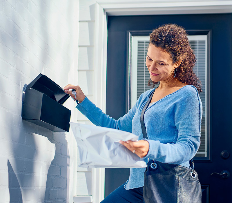 Woman stands next to mailbox with prescription package.
